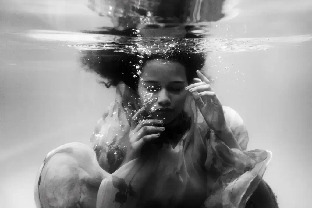 A black and white image of a woman in dress under water