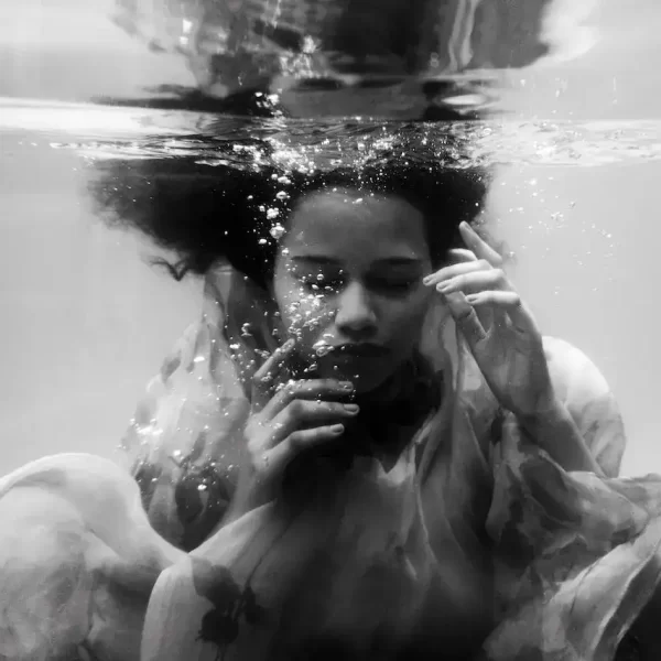 A black and white image of a woman in dress under water