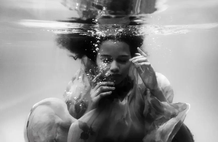 A black and white image of a woman in dress under water